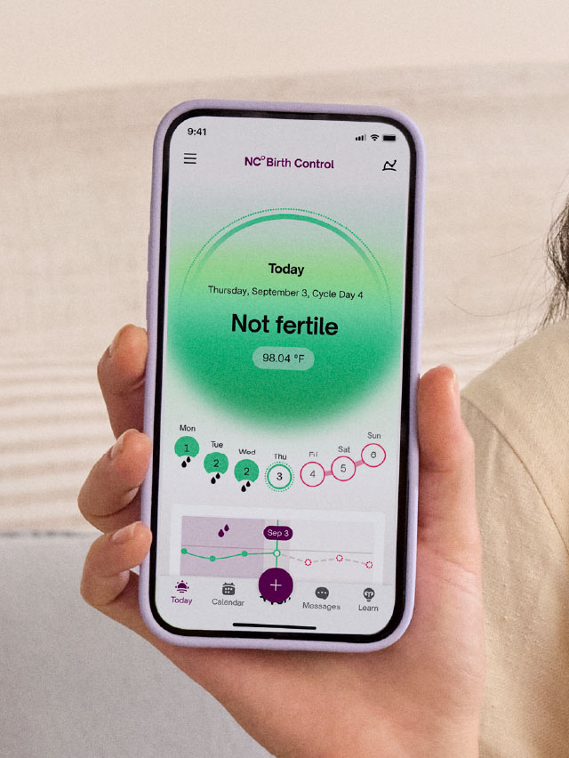 Photograph of a hand showing the Natural Cycles app today tab with the text 'Not fertile' on a green background. The App also shows upcoming Red Days, indicating the user's fertility status is about to change.