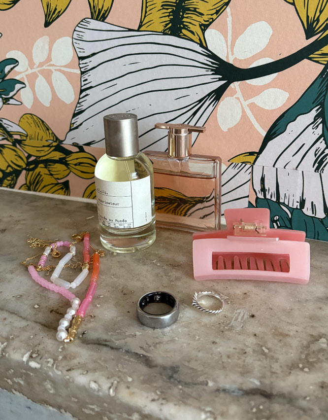 Photograph of Oura Ring next to a bottle of perfume a pink hair clip, a ring and a necklace