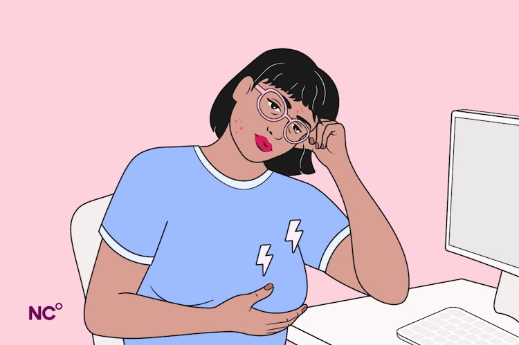 Woman sitting at her computer cupping her breast and looking pained