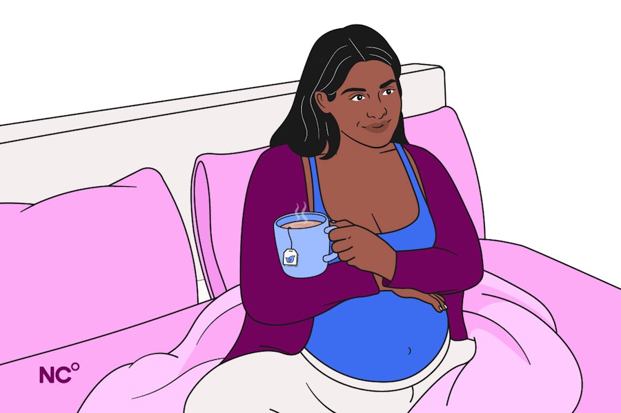 Pregnant woman sat in bed holding a cup of tea