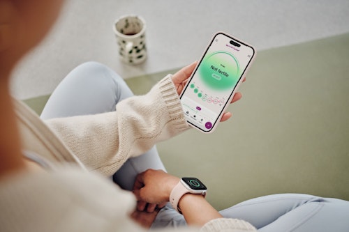 Woman wearing an Apple Watch and looking at her phone with the Not fertile screen in the NC° app