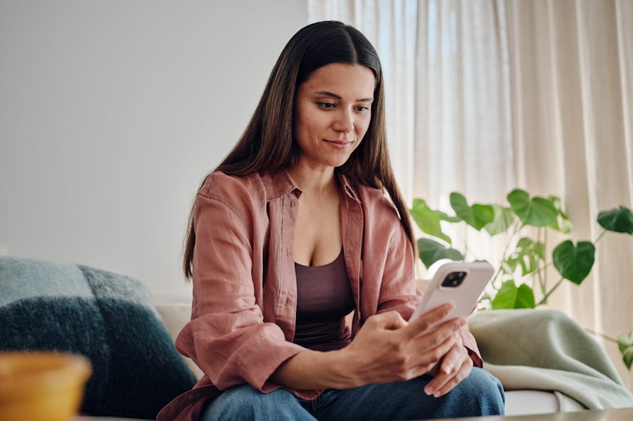 Woman with long dark hair sat on her sofa looking at her phone