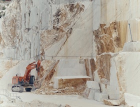 Excavator dwarfed by cut white marble walls in a quarry