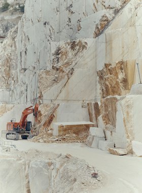 Excavator dwarfed by cut white marble walls in a quarry
