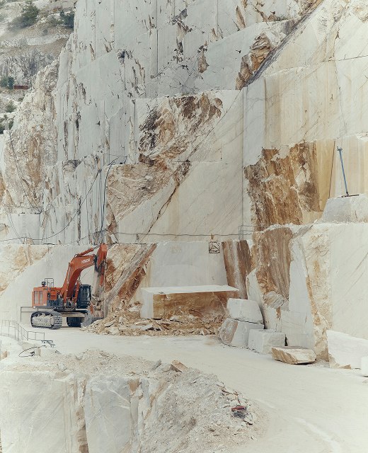 Excavator dwarfed by cut white marble walls in a quarry