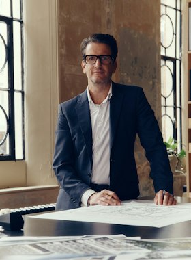 Squire & Partners architect in glasses standing at a desk covered in drawings