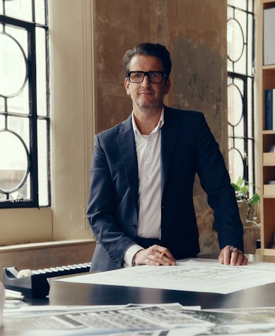 Squire & Partners architect in glasses standing at a desk covered in drawings