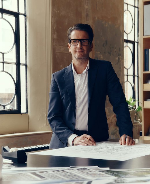 Squire & Partners architect in glasses standing at a desk covered in drawings