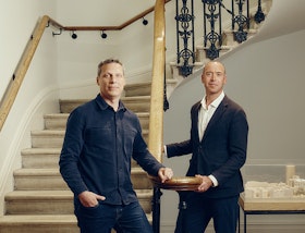 Two partners of EPR Architects standing beside a curved stone staircase with an ornate iron balustrade
