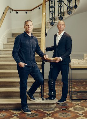 Two partners of EPR Architects standing beside a curved stone staircase with an ornate iron balustrade
