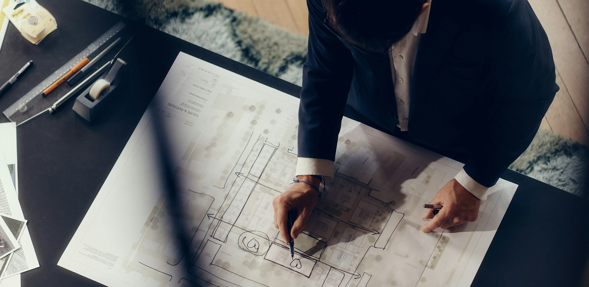 Overhead view of an architect sketching on a large site plan, softly blurred