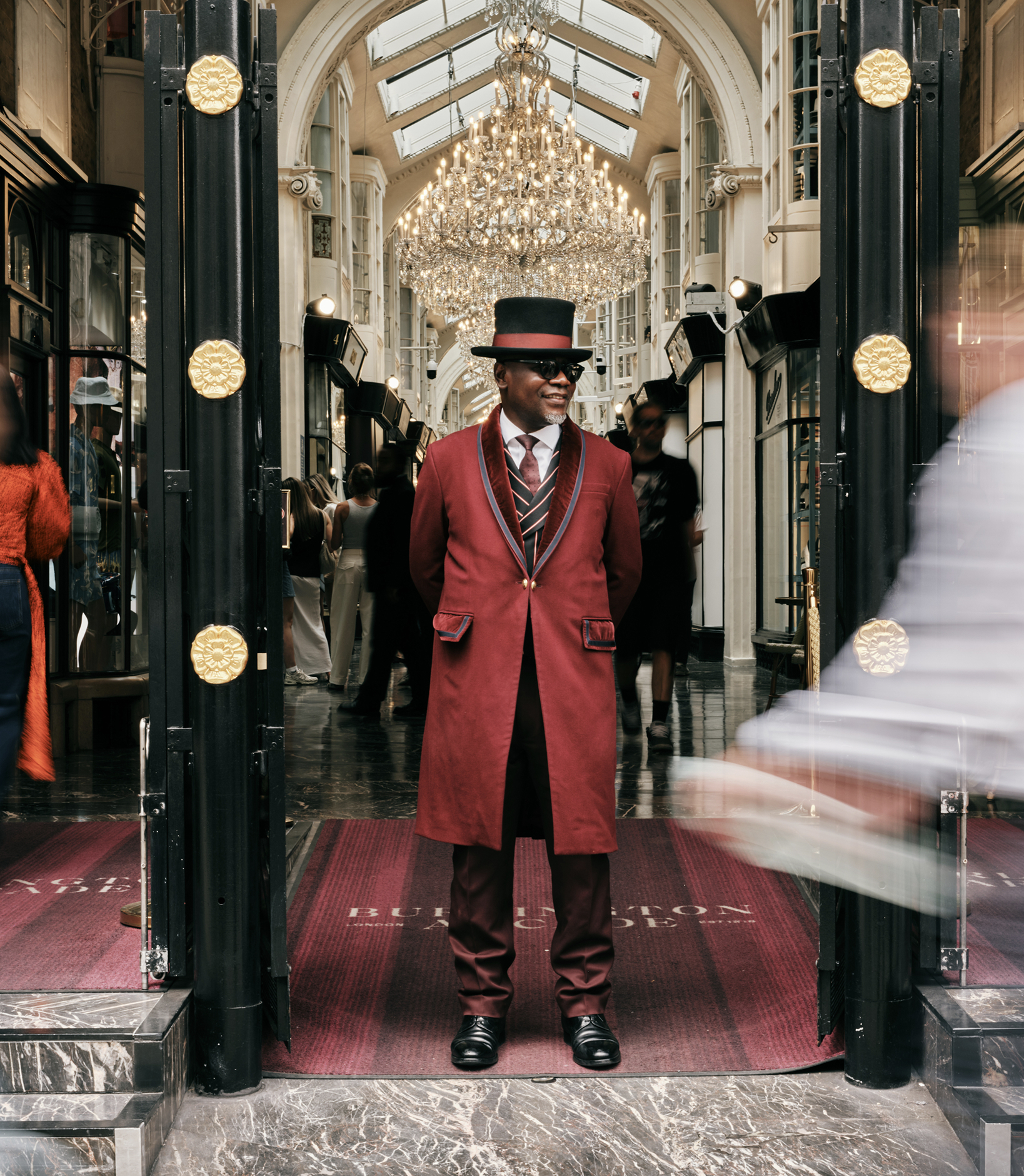 Beadle in a red frock coat and top hat at the entrance to Burlington Arcade beneath a chandelier