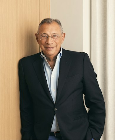 Sir George Iacobescu CBE, Executive Chairman, in a navy blazer leaning against an oak panel
