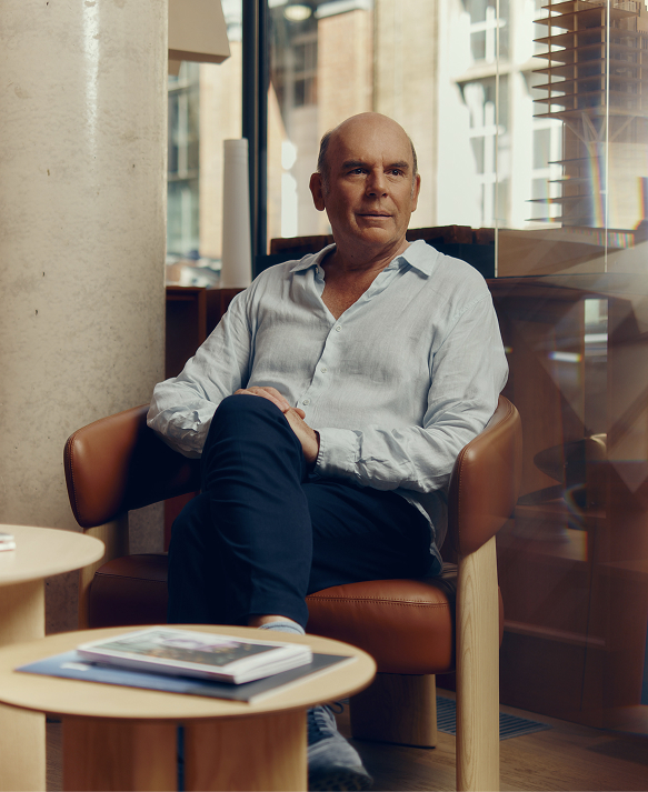 Man in a pale blue linen shirt seated in a tan leather armchair beside a window