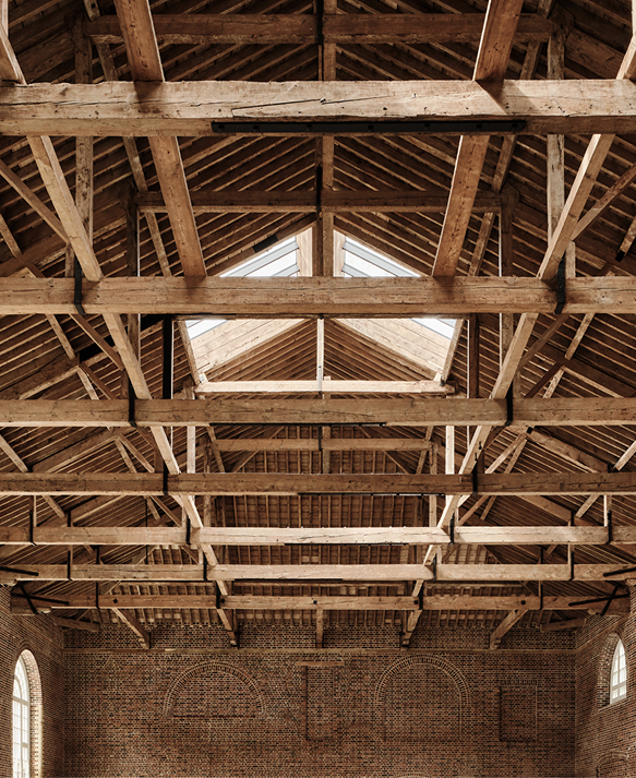 Exposed timber roof trusses and skylight above arched brick walls in the restored Riding School