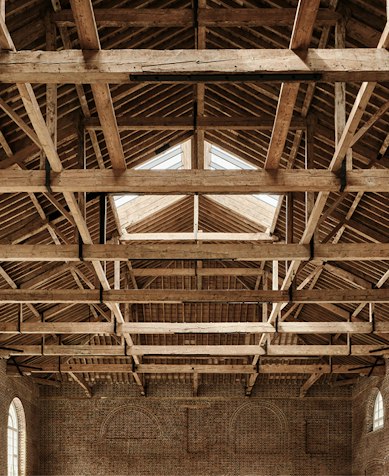 Exposed timber roof trusses and skylight above arched brick walls in the restored Riding School