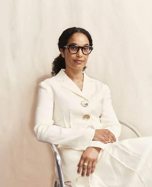 Portrait of Eva Langret of Frieze, seated in a cream suit against a draped backdrop