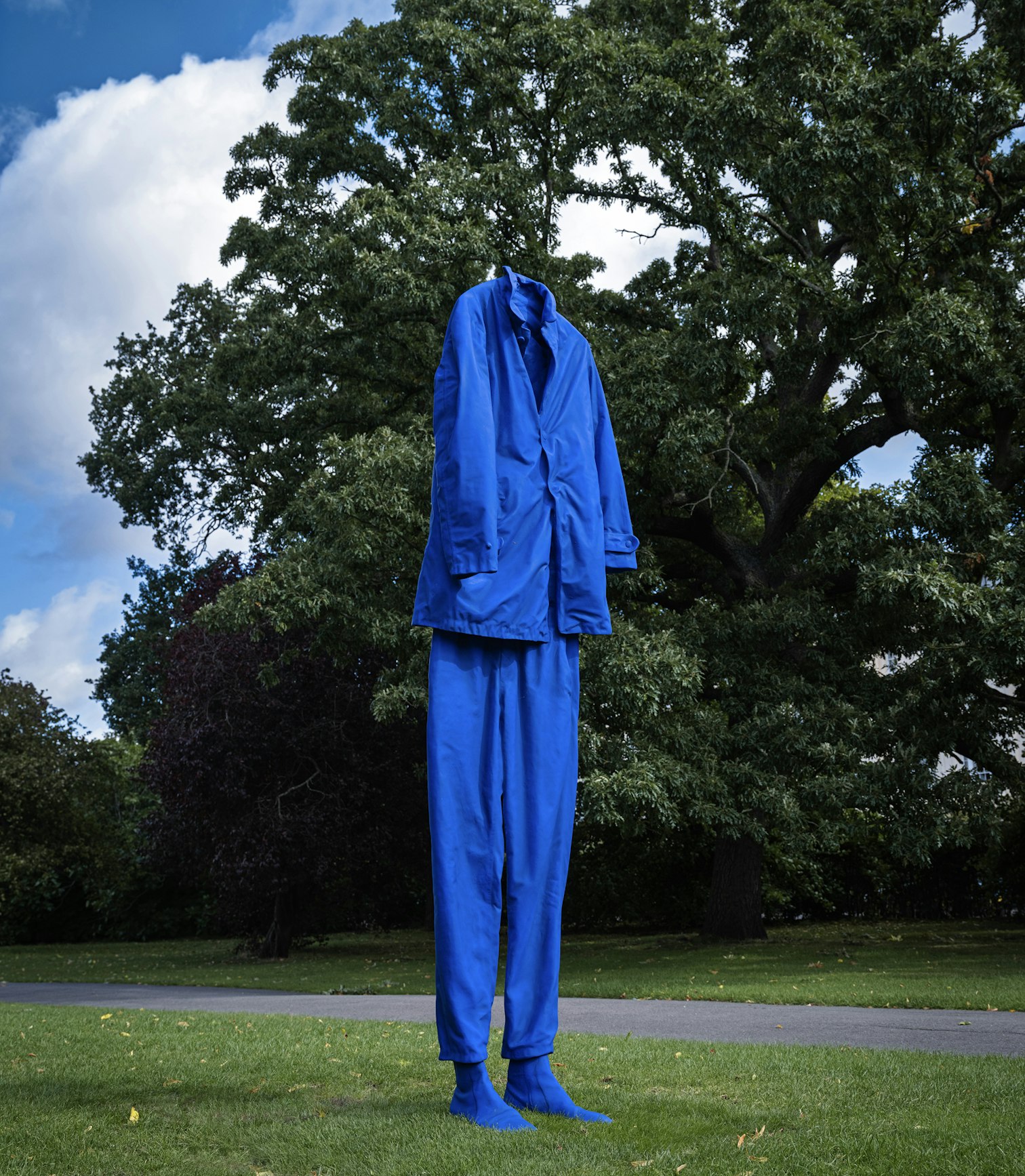Headless cobalt-blue suit sculpture standing on the grass beneath trees in the Regent's Park