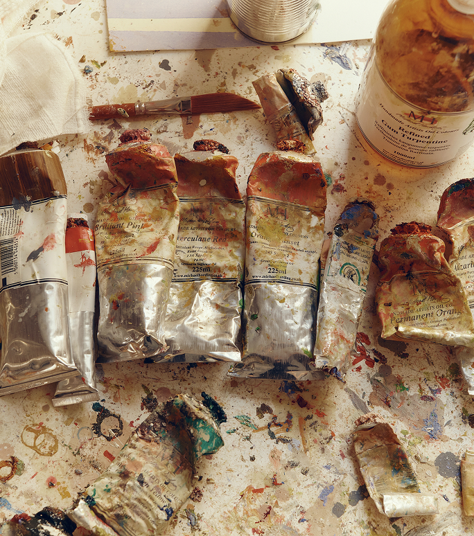 Used oil paint tubes and tins on a paint-splattered studio table