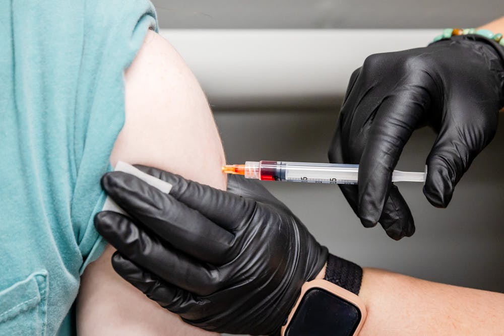 A Lume provider's hands in black medical gloves delivers an injection of vitamins into a client's upper arm. The supplement also includes glutathione in Chicago.