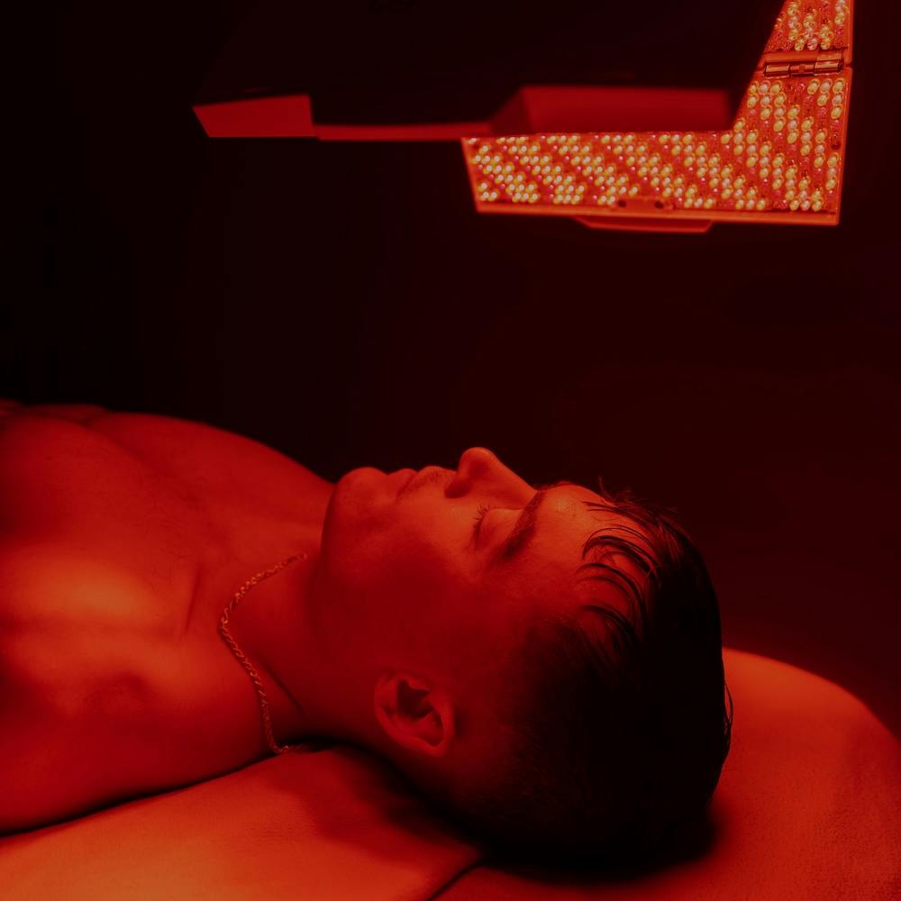 A male guest lies on a comfortable treatment bed as his face and shoulders ar ebathed in red light. This works as part of his treatment plan for facial rejuvenation in Chicago.