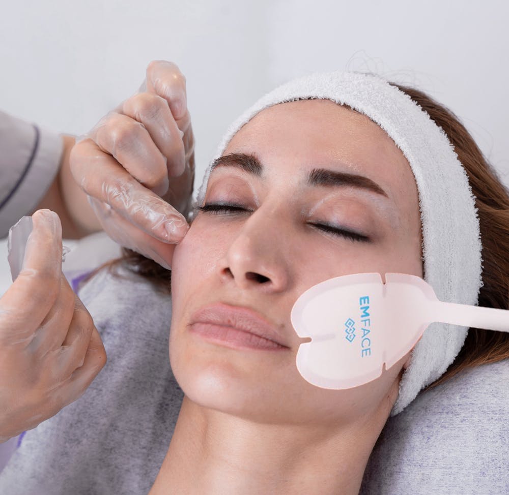 A Lume provider's gloved hands place an Emface applicator on a guest's cheek. The female guest is having Emface near Lincoln Park Chicago treatment to help contour her face for smoother skin and improved cheek appearance.
