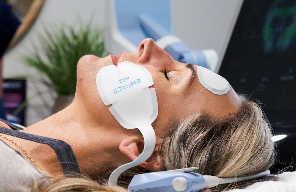 Sideview of the head of a female guest at Lume as she relaxes, eyes closed, on a treatment table. She has applicators attached to her cheeks and forehead as she receives facial contouring treatment through Emface near Lincoln Park Chicago.