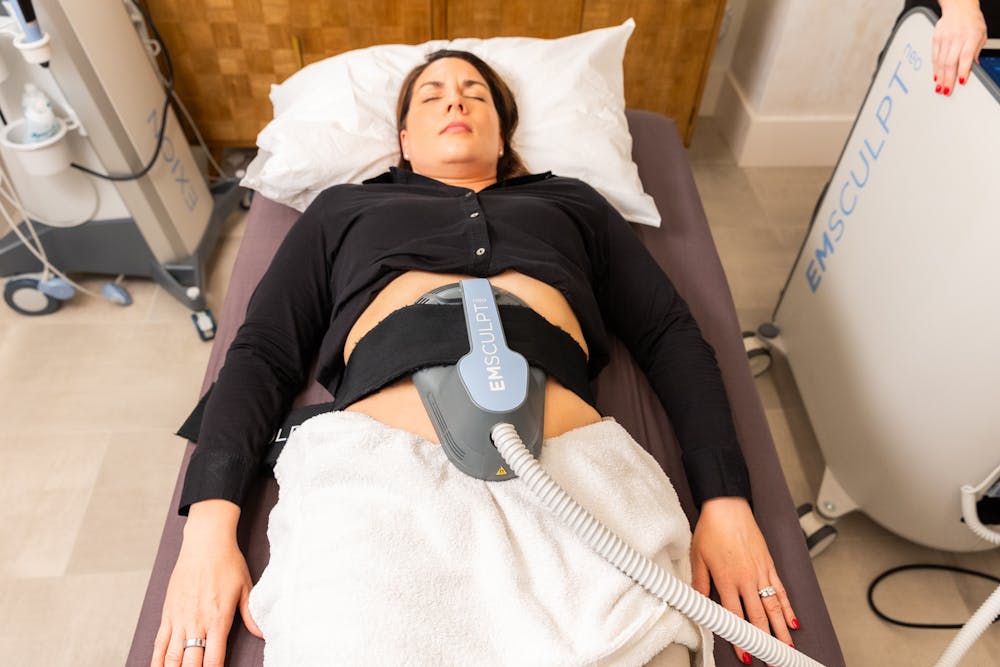 A woman lies down with an Emsculpt NEO applicator attached to her abdomen as a form of skin tightening after weight loss in Chicago.