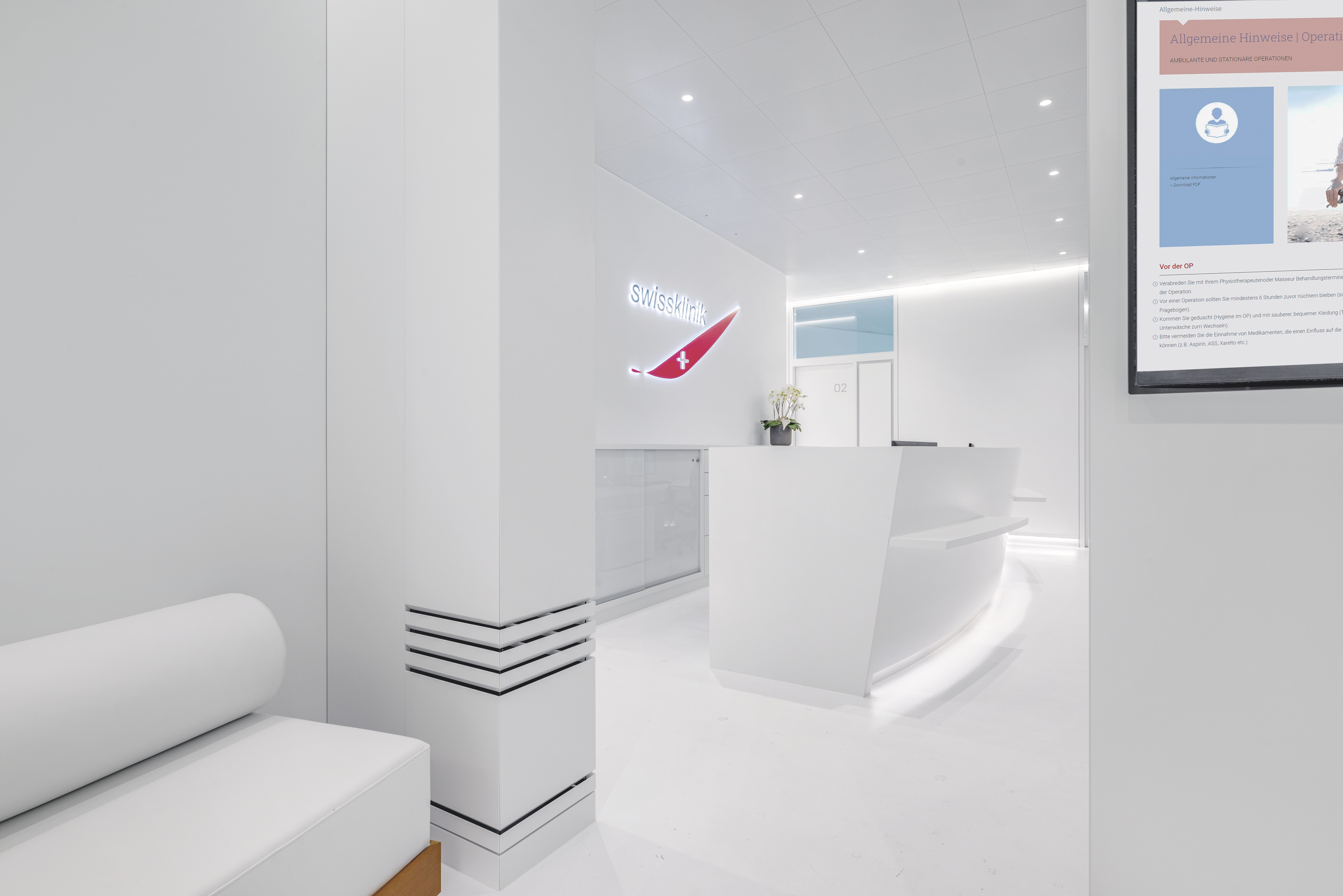 White reception desk at SwissKlinik Pfäffikon SZ with illuminated logo and waiting bench