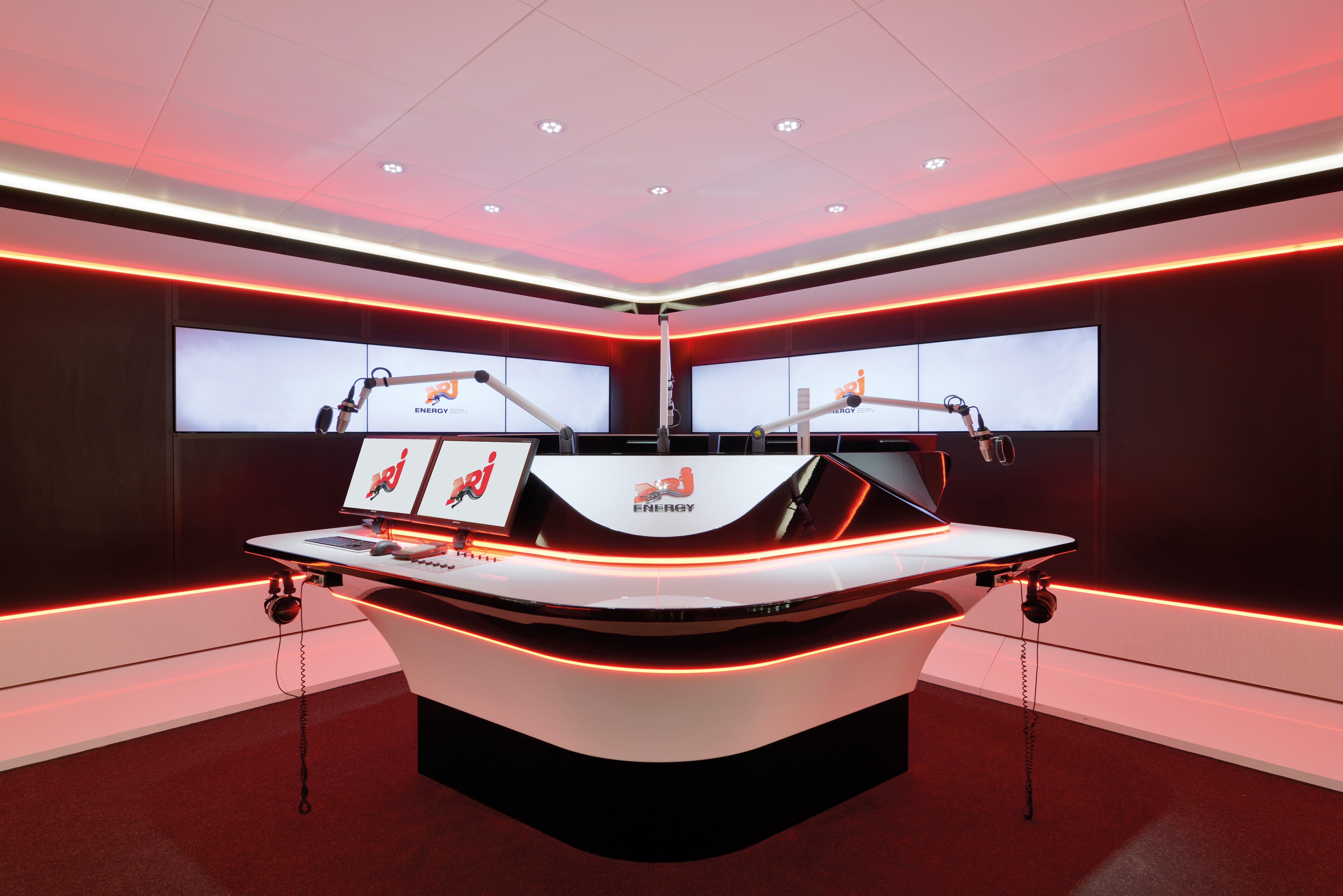 Radio NRJ Bern broadcast studio with a curved presenter desk in red lighting