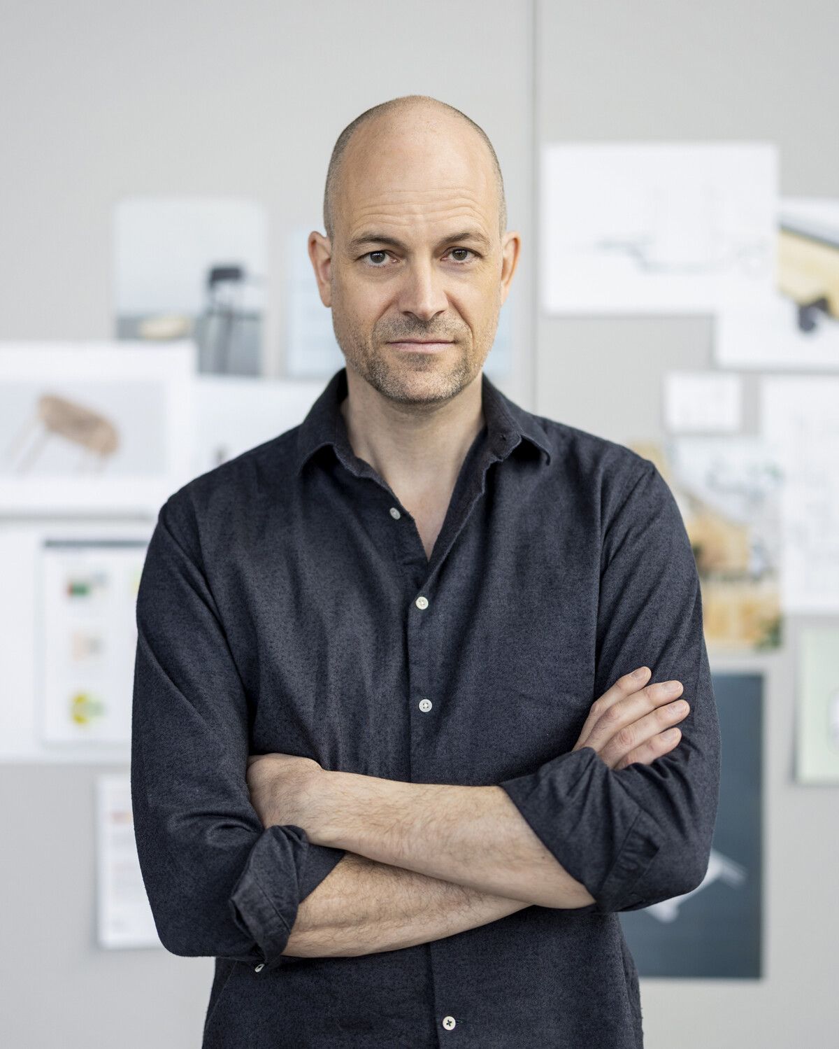 Portrait eines Designers mit verschraenkten Armen vor einem Moodboard mit Skizzen