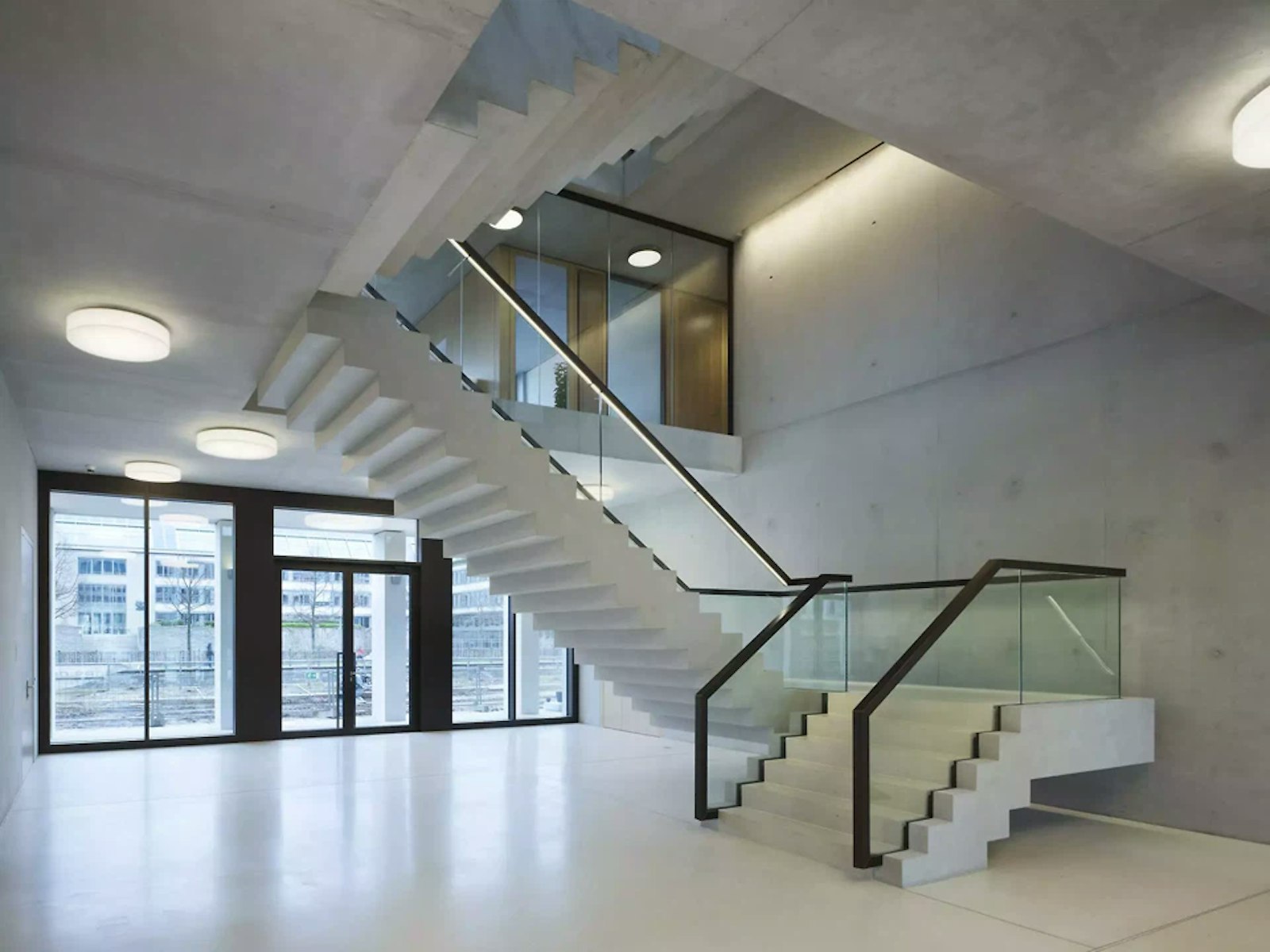 Hall d'entrée avec escalier en béton apparent, garde-corps vitré et fenêtres toute hauteur au Hamburger Bahnhof, Berlin