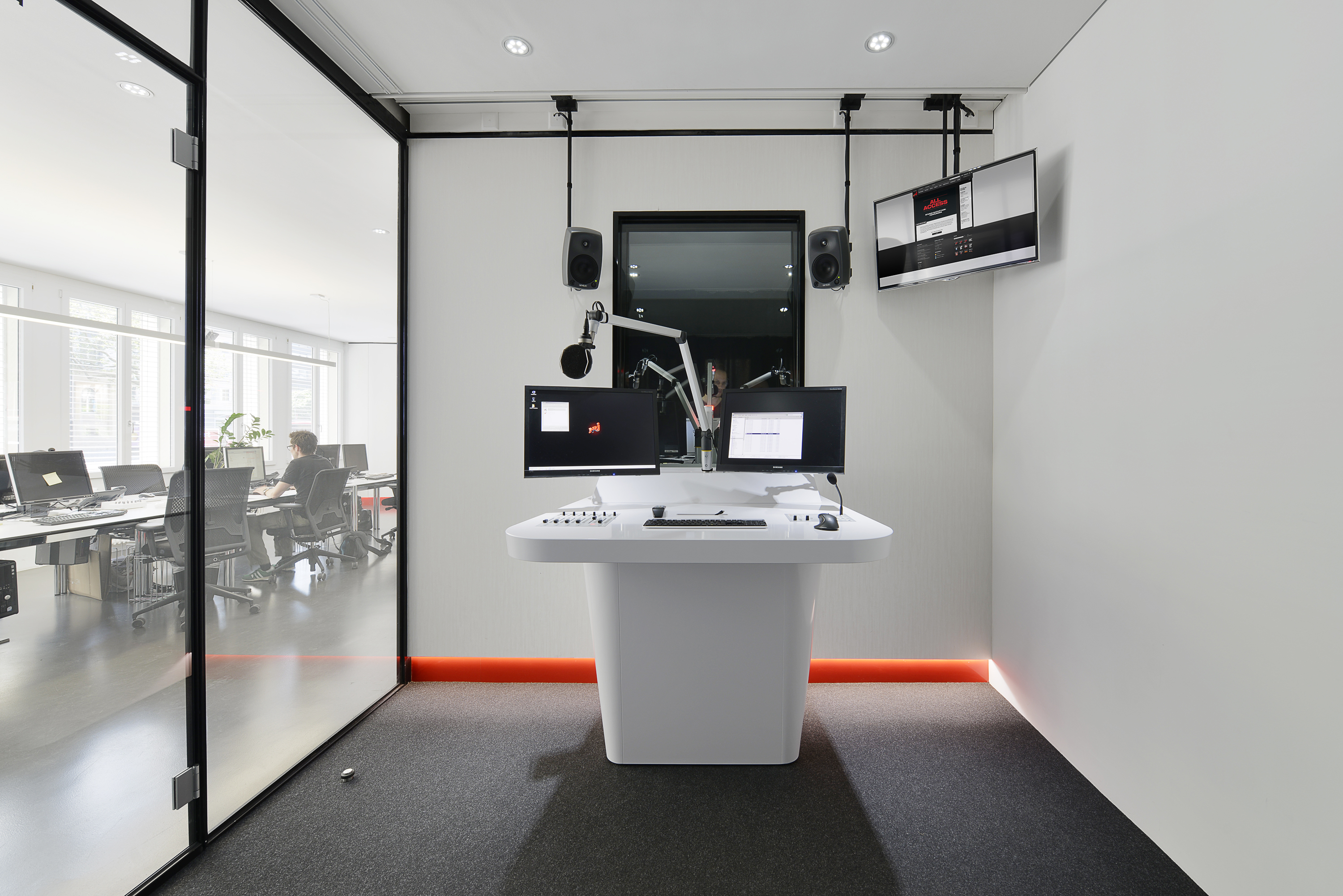 White broadcast desk with red LED strip and monitors in the Radio energy studio