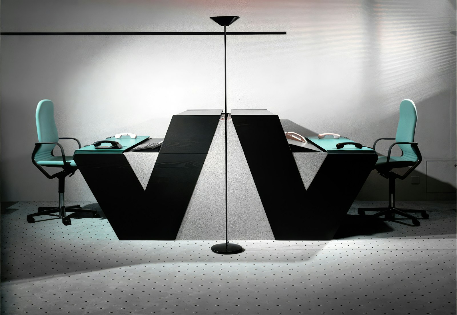 Two glossy black V-shaped control desks with teal office chairs, a 1988 design study