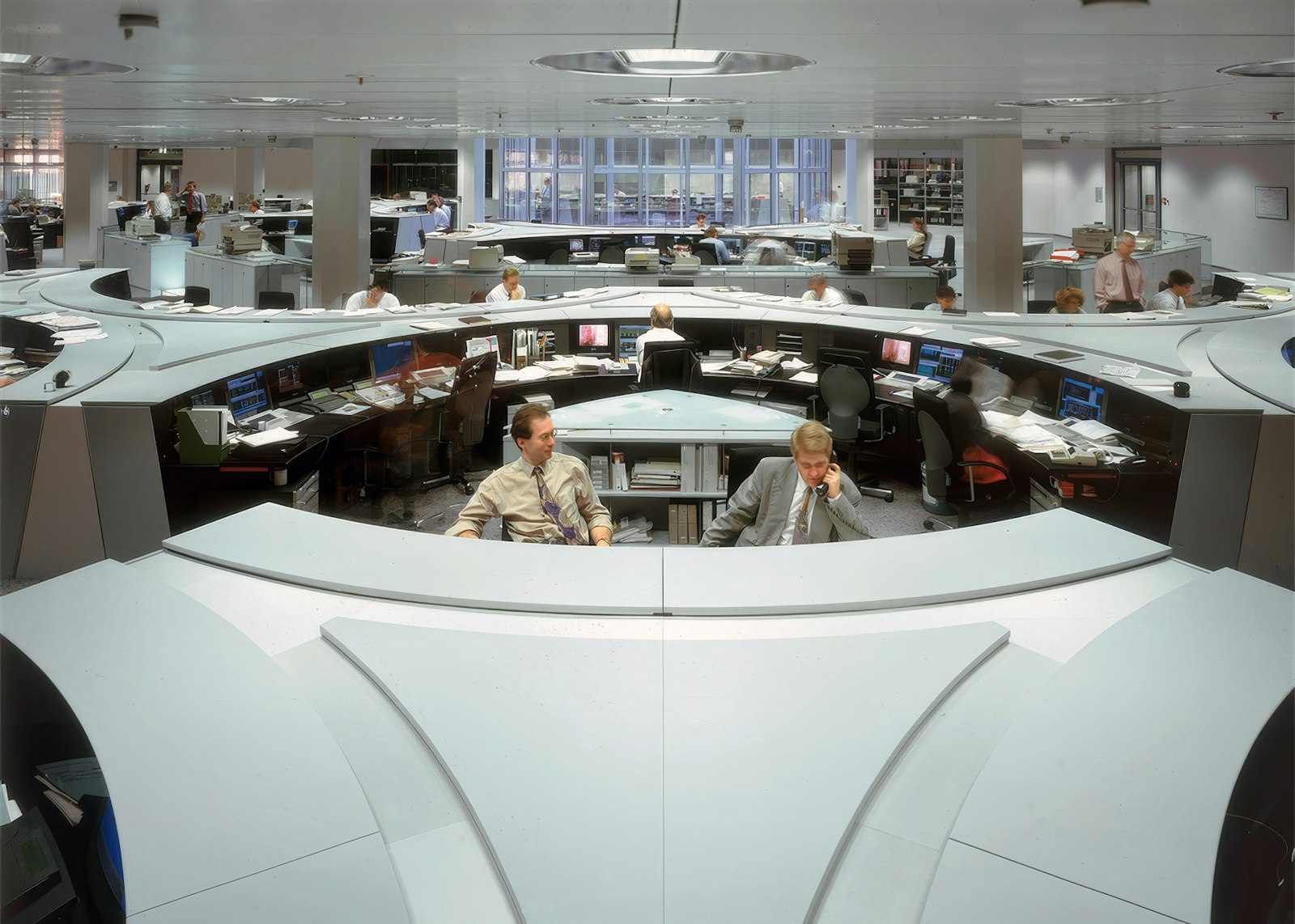 Oval trading-floor desks with several dealers and monitors in an open-plan office