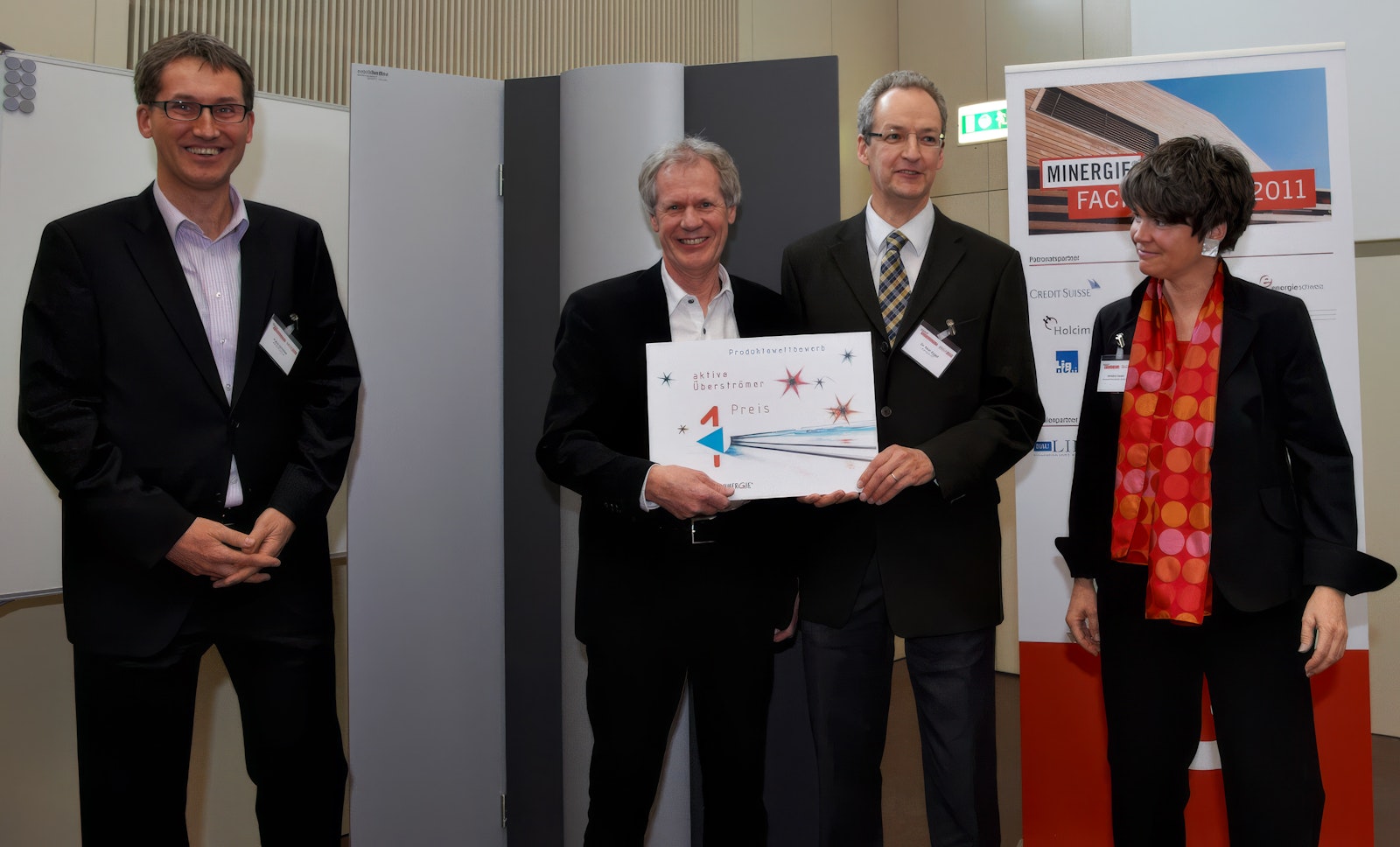 Four people at an award ceremony, with a Minergie conference poster from 2011 in the background