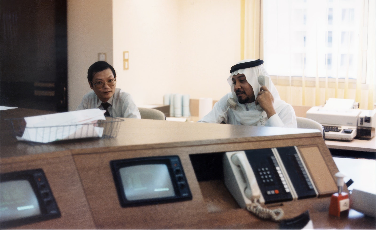 Clients in discussion at a control desk with monitors, international project from 1983