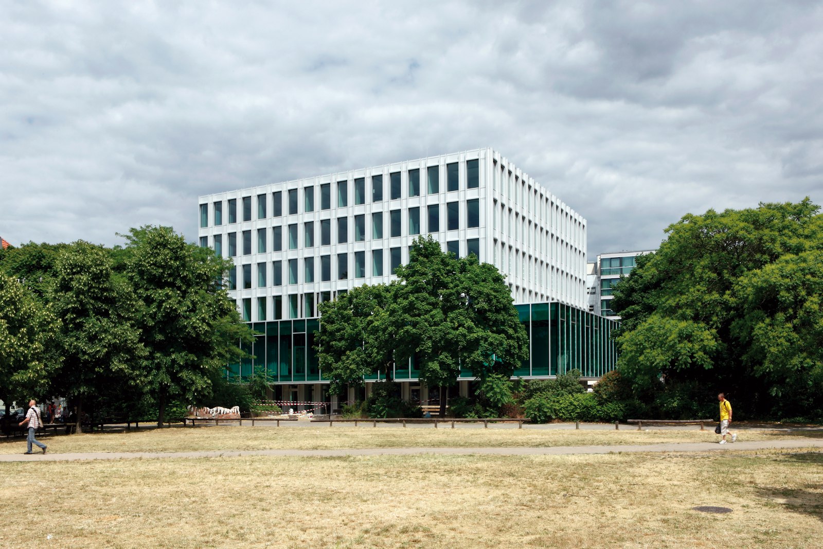 Modern office building with a light-coloured facade, surrounded by trees in a park