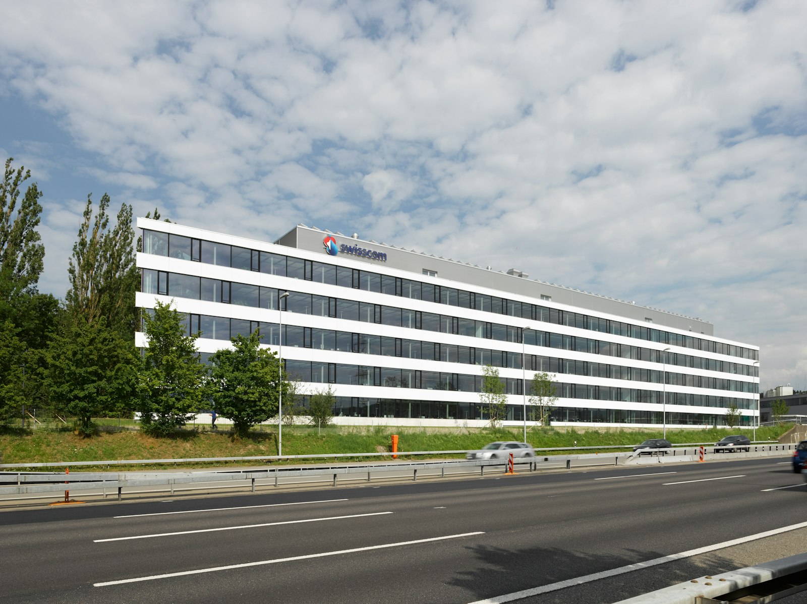Office building with Swisscom signage on the facade, seen from an adjacent motorway