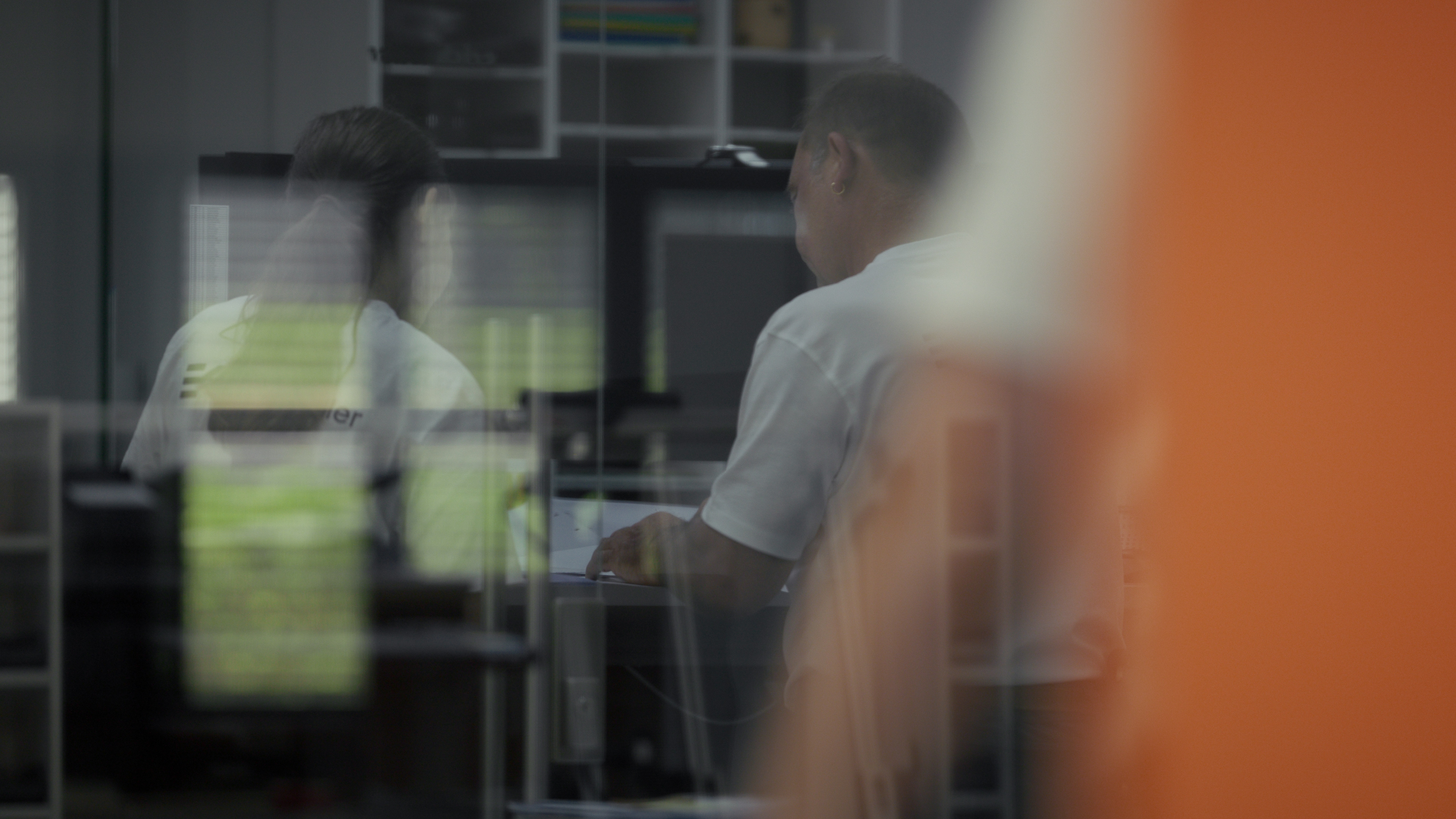 Spiegelung von Mitarbeitenden an Bildschirmarbeitsplätzen im Büro, durch Glas fotografiert