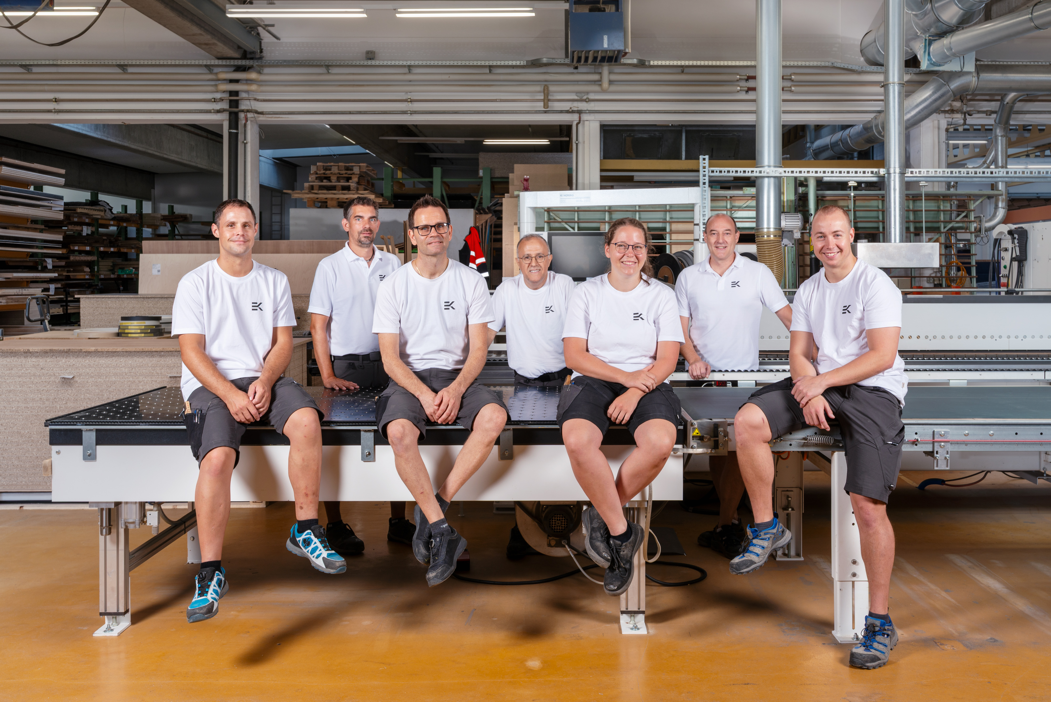 Team von Erich Keller sitzt auf einer Plattensäge in der Produktionshalle