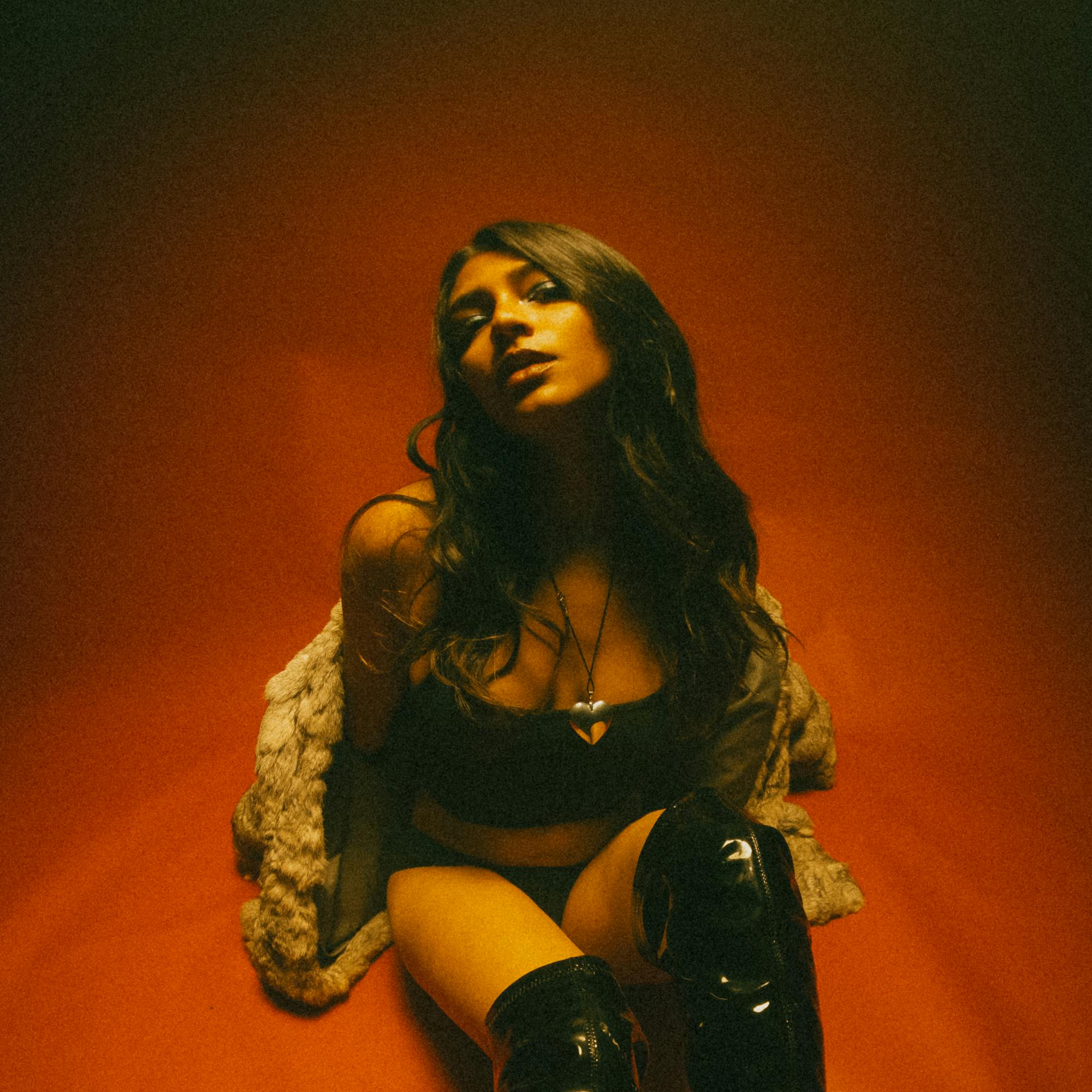Avara sitting on the floor in front of a faded orange background