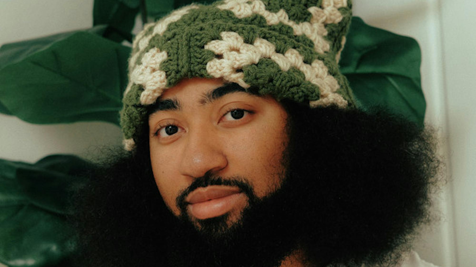 A closeup of L.Dre's face with a plant visible behind him