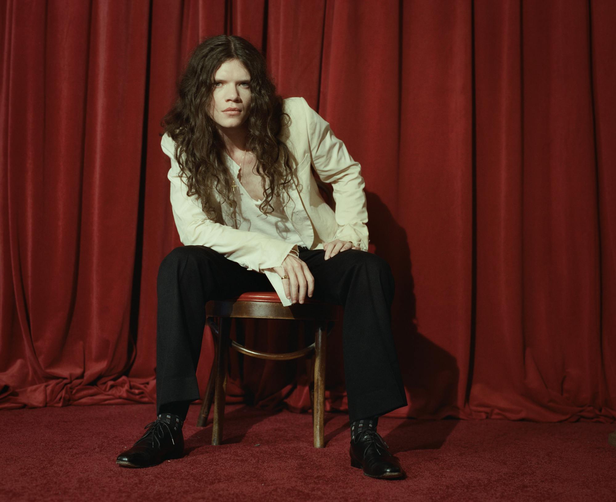 Sawyer Hill sitting on a stool in front of a red curtain