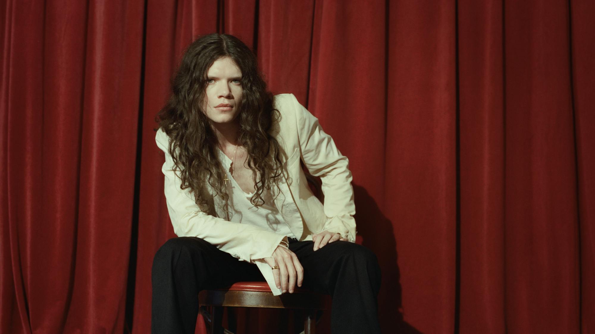 Sawyer Hill sitting on a stool in front of a red curtain