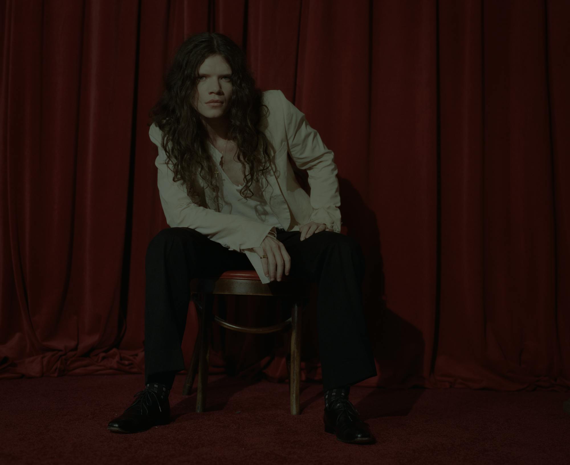 Sawyer Hill sitting on a stool in front of a red curtain