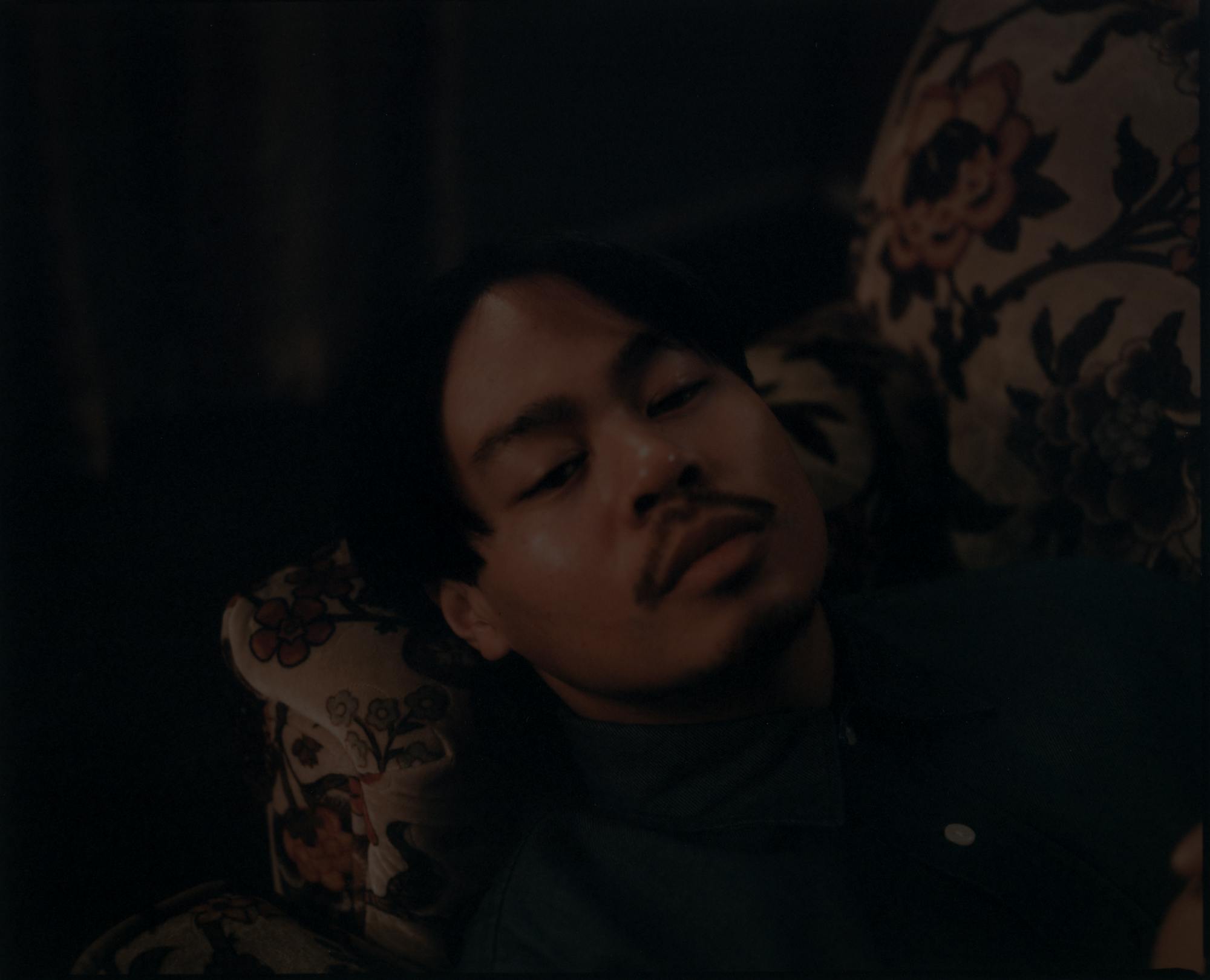 Closeup of Labit's face with his head resting on the arm of a couch with floral print