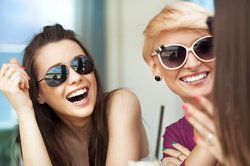 Two women wearing sunglasses, smiling with bright, white teeth 