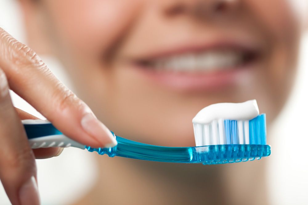 Close up of a hand holding a toothbrush with toothpaste on top of its soft bristles