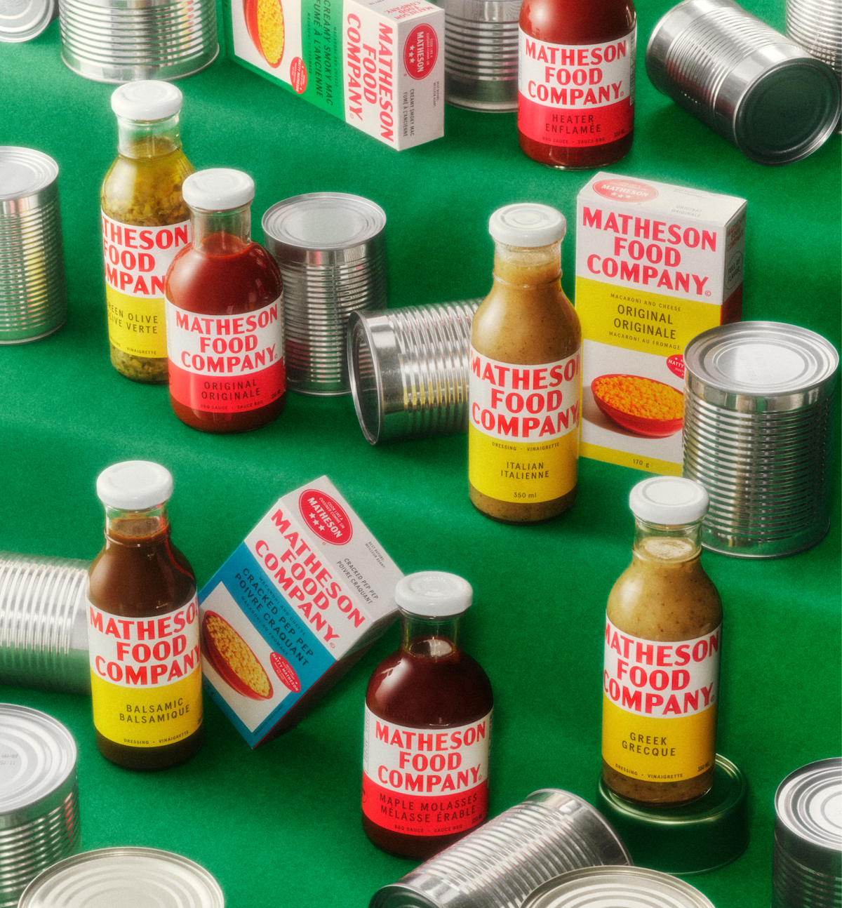 Matheson Food Company sauces, dressings and macaroni packaging arranged with metal cans on a green background.